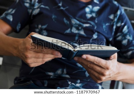 closeup of a young caucasian man reading a book at the waiting room of a train or bus station, or an airport