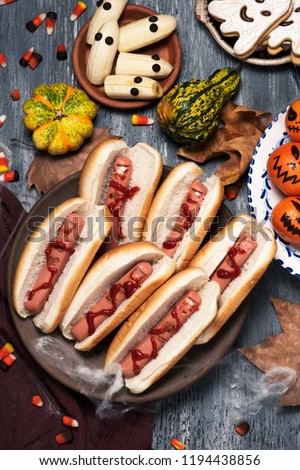 high angle view of an assortment of funny halloween food, such as hotdogs in the shape of bloody fingers, tangerines as carved pumpkins with funny faces or bananas with eyes as ghosts, on a table
