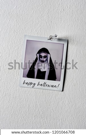 a picture of a frightening evil nun, wearing a typical black and white habit, with the text happy Halloween written in it, pinned to a white wall with a pushpin