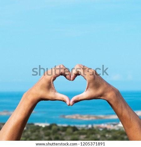 closeup of the hands of a young caucasian man forming a heart in front of the sea in the Southern coast of Corsica, in France