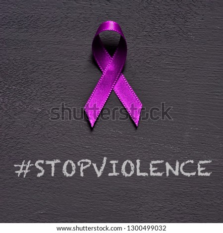 closeup of a purple ribbon, for the awareness about the unacceptability of the violence against women, and the text stop violence on a dark gray background