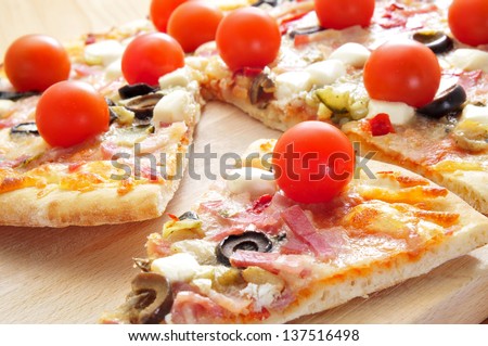 some slices of pizza with bacon, olives, cherry tomatoes, goat cheese, green pepper and eggplant