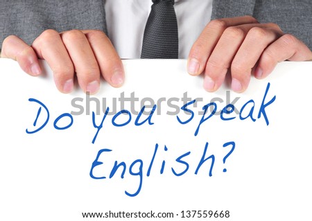 a man wearing a suit holding a signboard with the sentence do you speak english? written on it