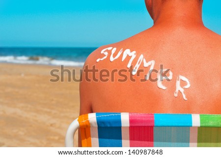 the word summer written with sunblock on the sunburnt back of a man who is sunbathing on the beach