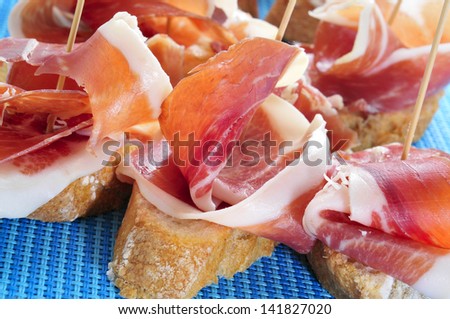 typical spanish pincho de jamon, spanish ham served on bread, on a blue background