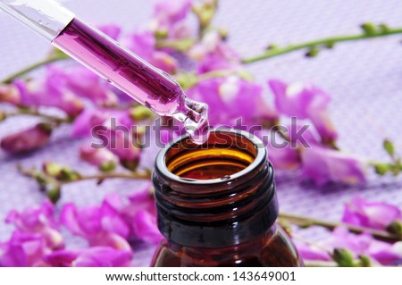 closeup of a dropper bottle and a pile of purple flowers on a purple background
