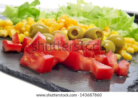closeup of some salad ingredients, such as tomato, olives, corn and lettuce, on a slate surface