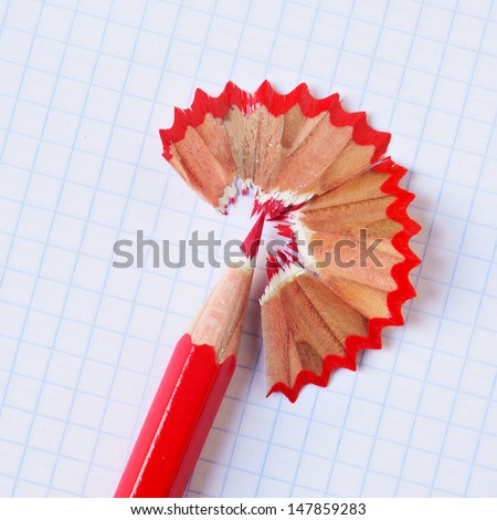 a sharpened red coloured pencil with its shavings on a checkered paper sheet