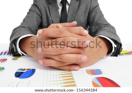 man wearing a suit sitting in a table full of charts with clasped hands