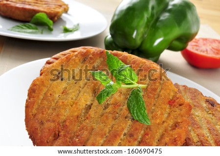 closeup of some veggie burgers in a plate on a table, with a green pepper and a tomato in the background