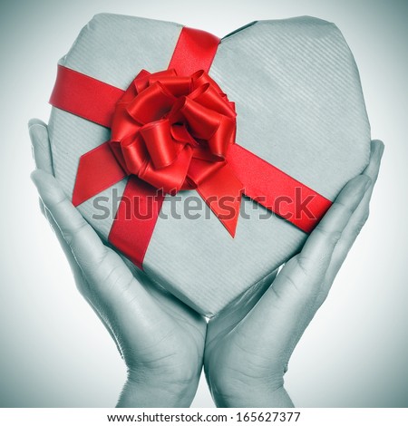 man hands holding a heart-shaped gift in black and white with a red ribbon