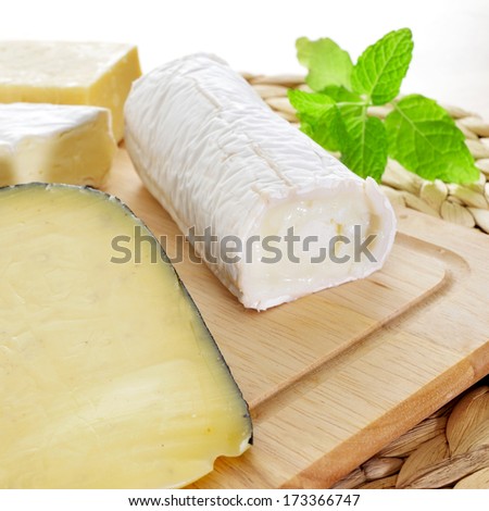 closeup of a wooden chopping board with an assortment of cheese, such as goat cheese, spiced cheese or Brie cheese