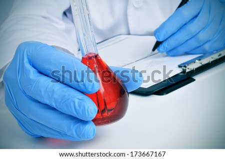 man in white coat with a volumetric flask with a red liquid in a laboratory