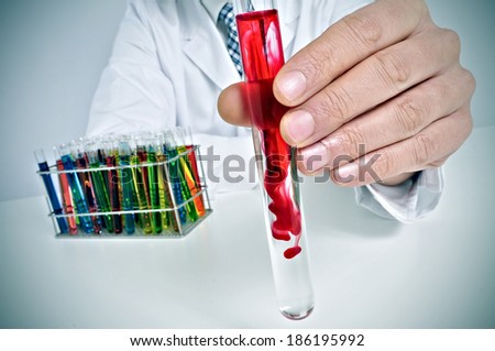 man in white coat sitting in a desk with test tubes with liquids of different colors in a laboratory