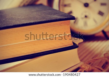 closeup of a pile of old books and an old alarm clock on a desk, with a retro effect