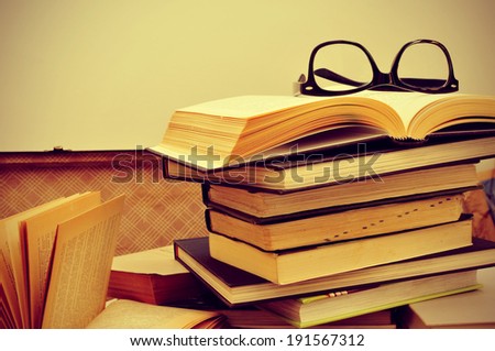 a pile of books and a pair of eyeglasses in an old suitcase, with a retro effect