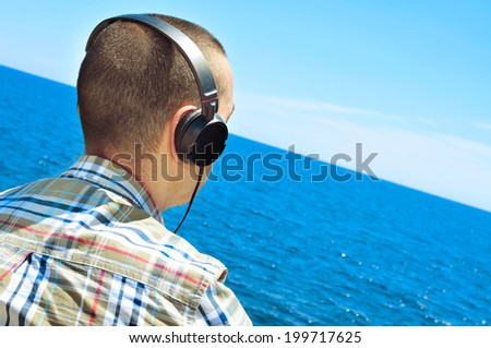 a young man listening to music with headphones in front of the sea