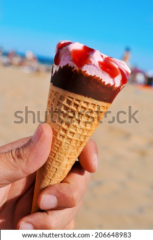 closeup of the hand of a man with an ice cream cone on the beach