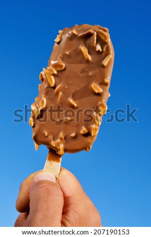 young man hand holding an appetizing chocolate ice cream over the blue sky