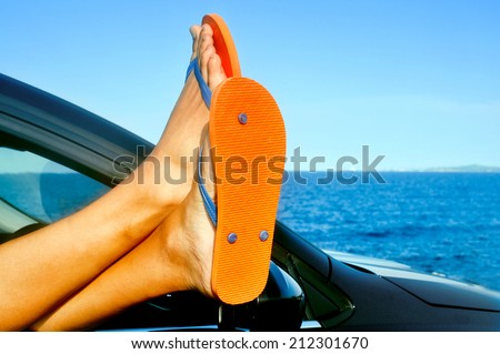 detail of the feet of a young man wearing flip-flops who is relaxing in a car near the ocean