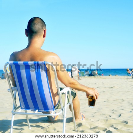 a young man hanging out on the beach, with a glass with cola drink
