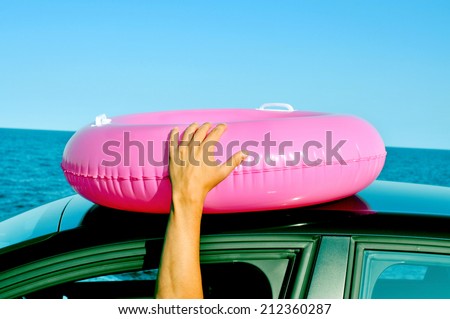 young man holding a swim ring on the top of a car getting his arm outside of the window