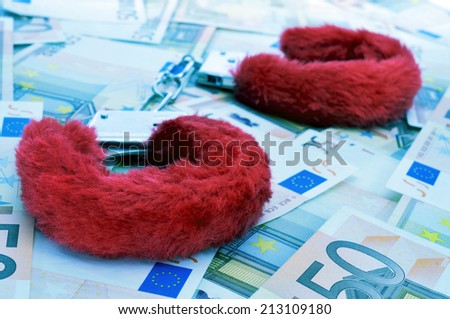 a pair of red sexy fluffy handcuffs on a pile of dollar bills depicting the idea of paying for sex or the sex industry or the sex commerce, with a filter effect