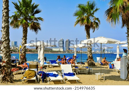 BARCELONA, SPAIN - AUGUST 19: Bathers lying in loungers in Sant Sebastia Beach on August 19, 2014 in Barcelona, Spain. In the background, Mapfre Tower and Hotel Arts, two of the landmarks in the city