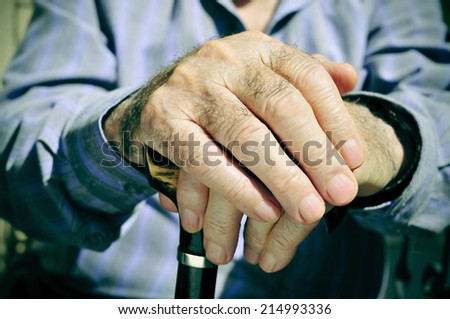 closeup of the hands of an old man with a walking stick