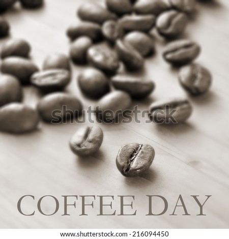 the text coffee day and a pile of roasted coffee beans on a wooden table, in duotone