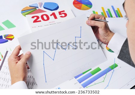 businessman in his office desk observing a chart with an upward trend, with a 2015 calendar in the background