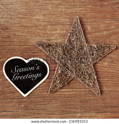 the sentence seasons greetings written in a heart-shaped chalkboard and a rustic christmas star on a wooden surface