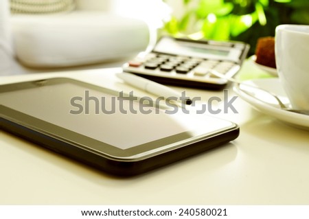 detail of a desk with a tablet, a calculator and a cup of coffee or tea in an office with a nice atmosphere