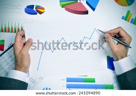 businessman in his office desk full of graphs and charts observing a chart with an upward trend