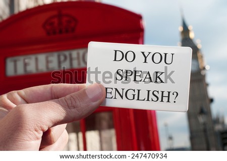 a man holding a signboard with the text do you speak english? with a red telephone booth and the Big Ben in the background, in London, UK