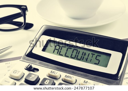 the word accounts written in the display of a calculator on an office desk, with a cup of coffee or tea in the background