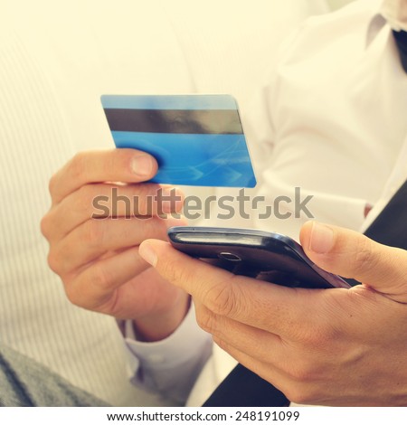 a young man in suit using his credit card to shop online with his smartphone