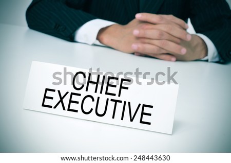 a man in suit sitting at a desk with a signboard in front of him with the text chief executive written in it