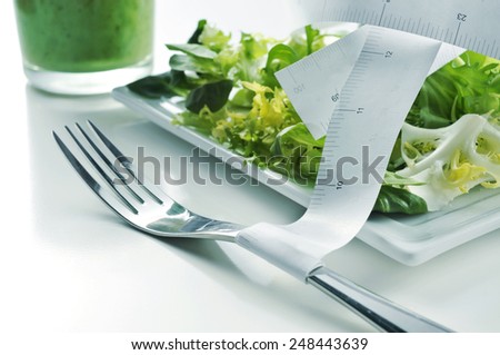 closeup of a plate with a green salad and a measuring tape and a green smoothie, depicting the concept of dieting or to stay fit