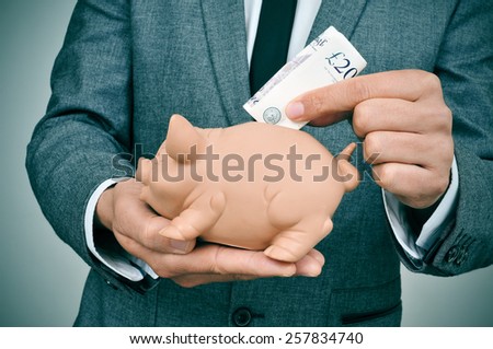 closeup of a young man wearing a suit introducing a pound sterling bill in a piggy bank