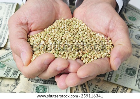 closeup of a pile of buckwheat seeds in the hands of a man on a background full of dollar banknotes, depicting the agribusiness concept