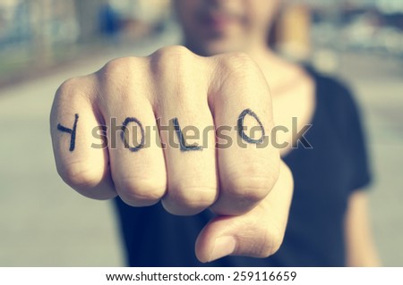 closeup of a young man with the word yolo, for you only live once, tattooed in his hand, with a filter effect
