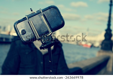 a sheltered young man taking a self-portrait with a selfie stick next to the River Thames in London, United Kingdom, with a filter effect