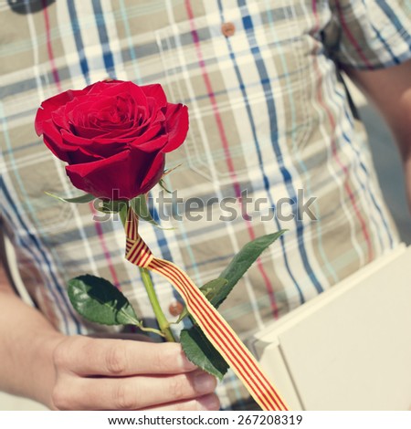 a young man with a red rose and the catalan flag, and a book for Sant Jordi, the Saint Georges Day, when it is tradition to give red roses and books in Catalonia, Spain