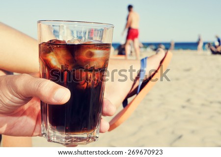 closeup of a young caucasian man hanging out on the beach with a glass with cola drink