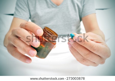 a young caucasian man in pajamas in bed about to take a blue pill from a brown bottle