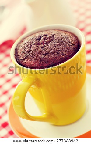 closeup of a chocolate mug cake in a yellow porcelain mug on a set table covered with a checkered tablecloth