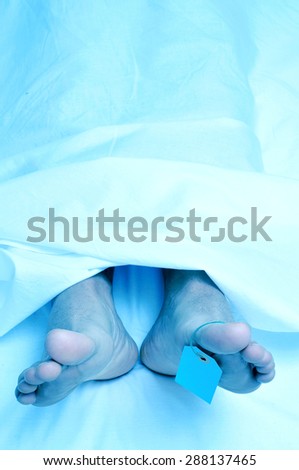 closeup of the feet of a dead body covered with a sheet and with a blank tag tied on the big toe of his left foot