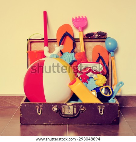an old cardboard suitcase full of beach items, such as diving masks, pails and shovels, a beach ball, sunblock or flip-flops, placed on the floor, with a retro effect