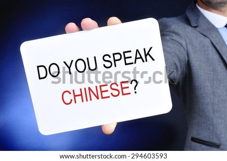closeup of a man in a gray suit showing a signboard with the question do you speak chinese? written in it